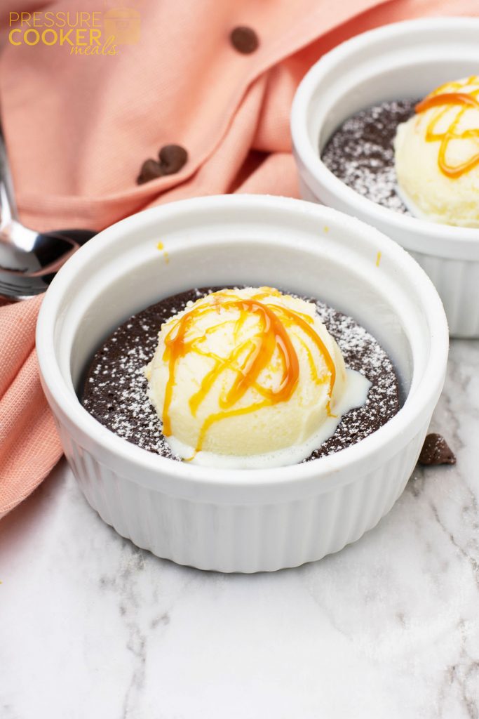 Instant Pot Brownie Cakes in ramekins dusted with powdered sugar, plus ice cream and caramel