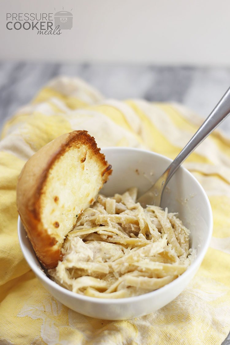 White bowl with Instant Pot Chicken Alfredo and Garlic Bread on a yellow cloth