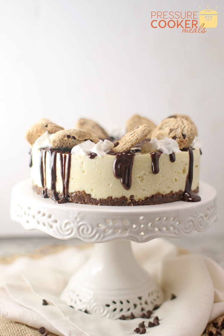 side view of Instant Pot Chocolate Chip Cookie Dough Cheesecake on cake stand with ganache and chocolate chip cookies