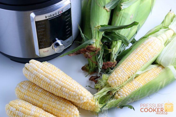 Fresh corn on the cob cleaned and uncleaned next to an Instant Pot